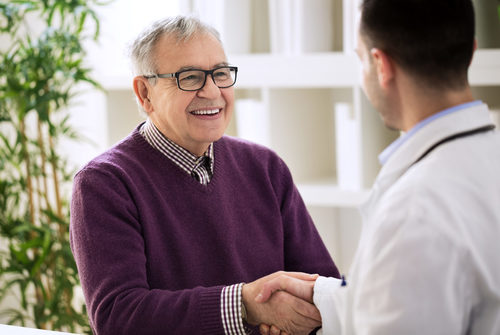 Smiling happy healthy old male shaking with doctor