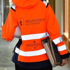 Person in orangefarbener Sicherheitsjacke mit Logo der Bauaufsicht Wiesbaden