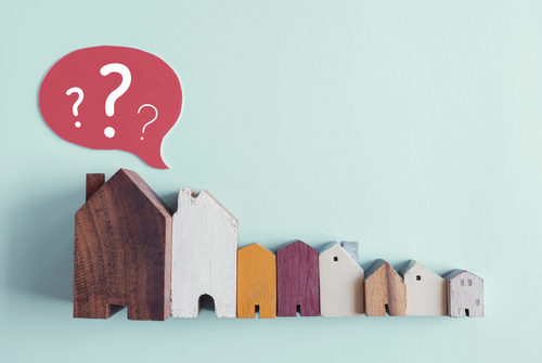 Kleine Holzhaus-Figuren mit einem Fragezeichen vor einem grünen Hintergrund