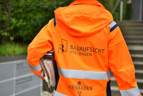 Oberkörper einer Person in orangener Sicherheitsjacke mit Logo der Stadt und der Bauaufsicht Wiesbaden