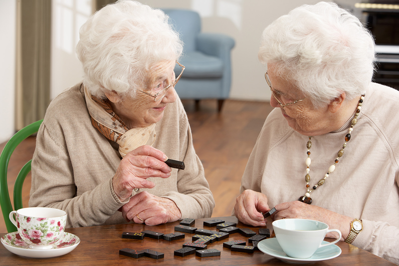 Zwei Seniorinnen unterhalten sich am Tisch sitzend bei einem Domino-Spiel.