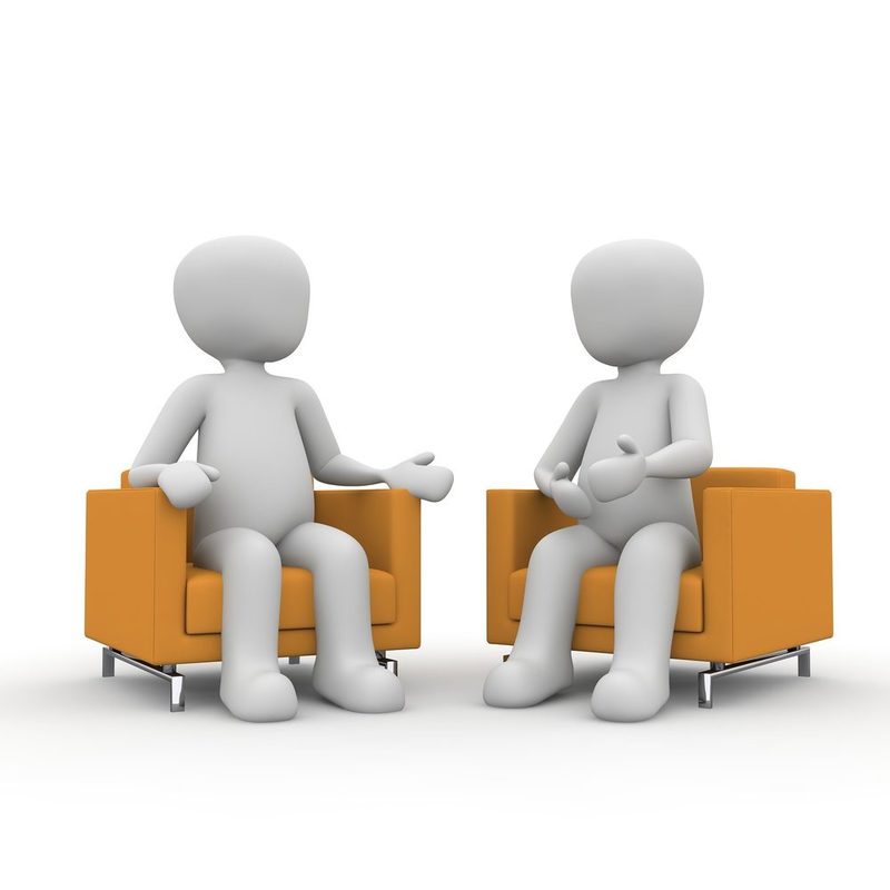 Zu sehen sind zwei stilisierte Menschen , die sich gegenübersitzen und miteinander sprechen.