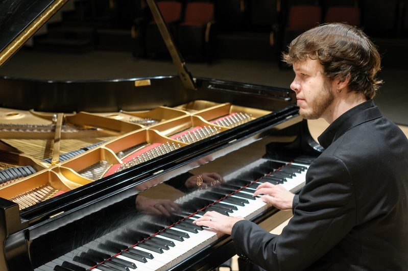 Ein Mann mit braunen Haaren sitzt an einem Flügel und spielt Klavier.