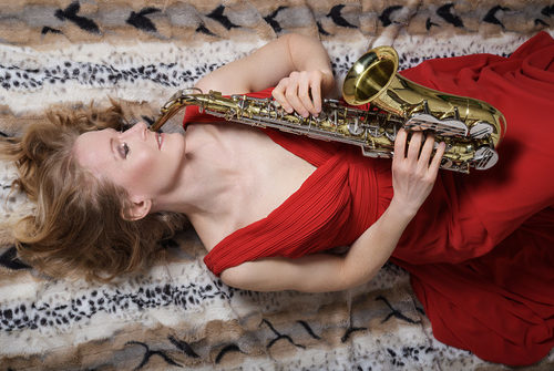 blonde Frau in rotem Kleid liegt auf dem Boden mit einem Saxofon in den Händen haltend