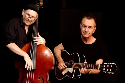 Links steht ein Mann mit einem Cello und rechts neben ihm sitzt ein Mann mit einer Gitarre.