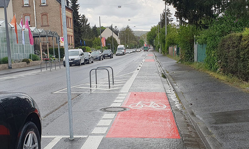 Rot-schwarzer Radweg entlang einer Autostraße.