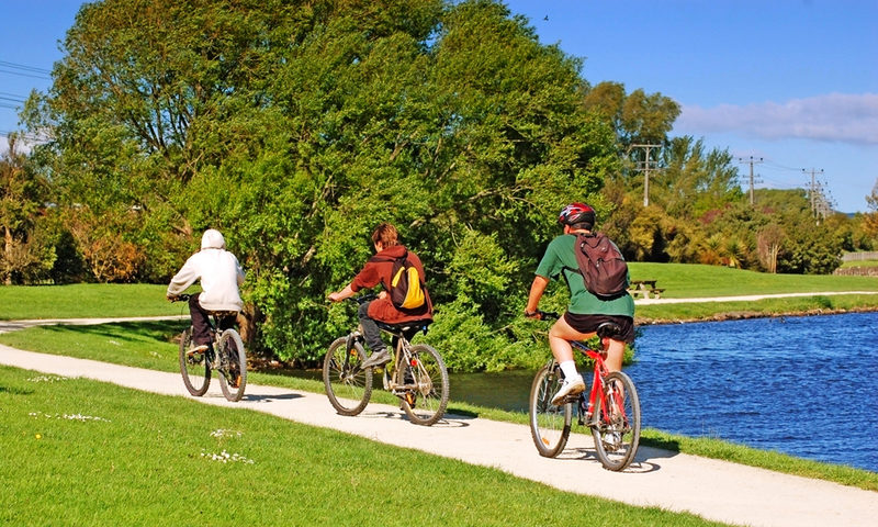 Fahrräder mieten - hier drei Radfahrer im Park am Wasser unterwegs.