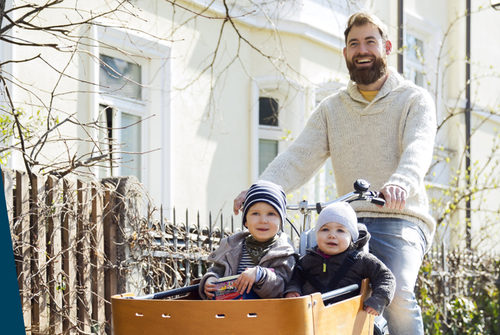 Mann auf einem Lastenrad mit zwei Kindern als "Beifahrer".